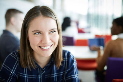 Close-up of smiling woman looking away while sitting at university cafeteria