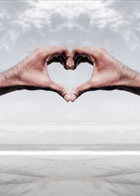 Cropped hands making heart shape at beach against sky