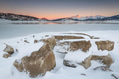 Snow covered shore against sky during sunset