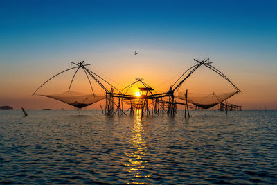 Silhouette cranes against sea during sunset