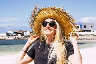 Portrait of smiling young woman wearing sunglasses against sky