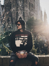 Young man holding coffee cup while sitting against sagrada familia