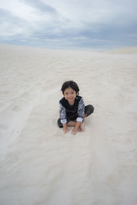 Portrait of smiling girl playing with sand at beach against cloudy sky