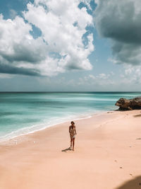 Woman walking at beach against cloudy sky