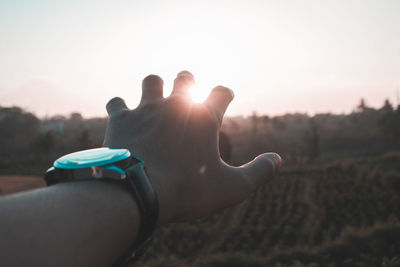 Cropped image of hand wearing wristwatch during sunset