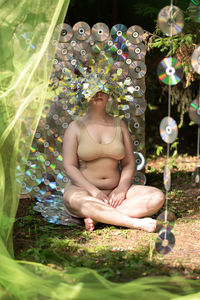 Portrait of shirtless young woman sitting on field