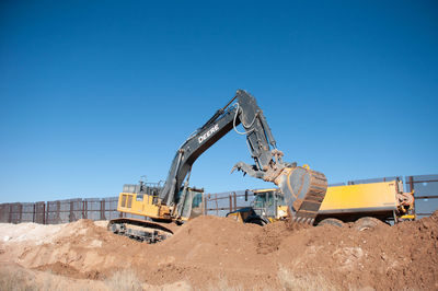 Cranes at construction site against clear blue sky