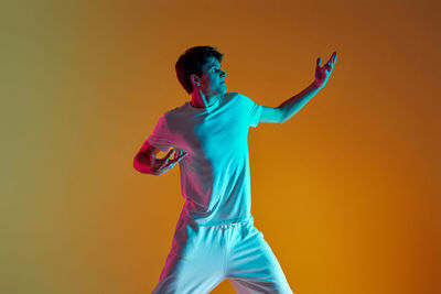 Portrait of young man playing with arms raised standing against wall