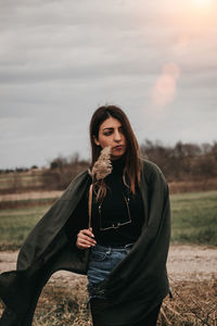 Portrait of beautiful woman standing on field against sky