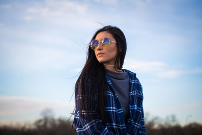 Portrait of young woman wearing sunglasses standing against sky