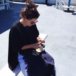 Woman having food while sitting on bench in city