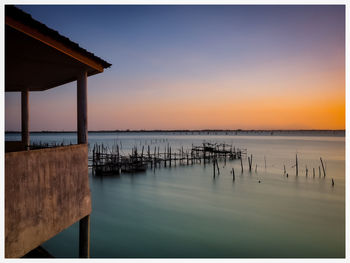 Wooden posts in sea against sky during sunset