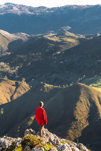 Back view of anonymous explorer standing on green rock and admiring picturesque landscape of mountains in el mazuco