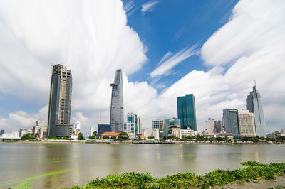 River by modern buildings in city against cloudy sky