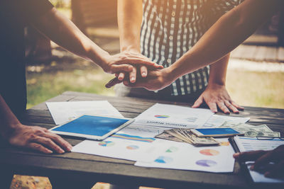 Midsection of colleagues stacking hands by charts and paper currency on table