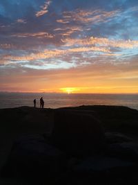 Silhouette people standing on beach against sky during sunset