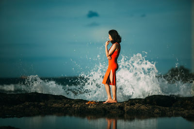 Full length of young woman standing at beach against sky