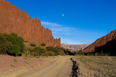 Dirt road amidst rocky mountains against sky