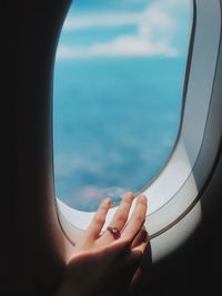 Cropped image of hand by airplane window in sea