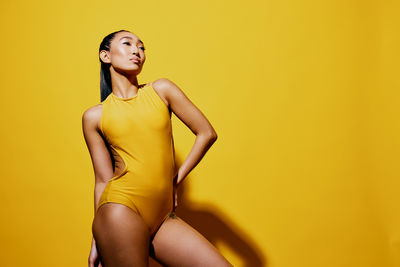 Portrait of young woman standing against yellow background