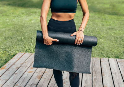 Midsection of woman holding exercise mat while standing outdoors