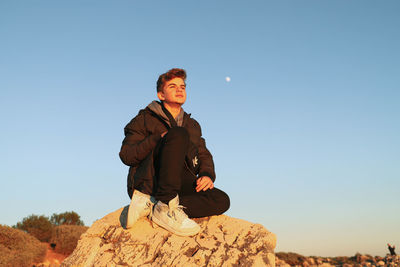 Man sitting on rock against clear sky