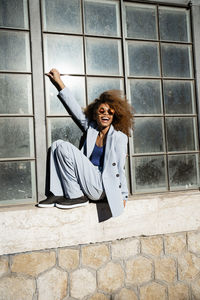 Cheerful young woman sitting while balancing on window sill