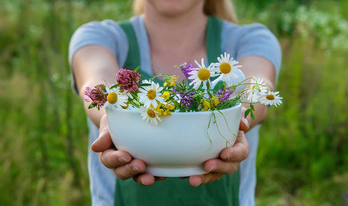Midsection of woman showing flowers in mortar