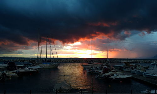 Sailboats moored at harbor against cloudy sky