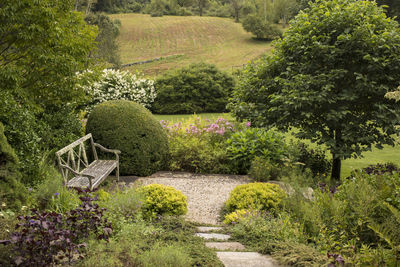 A weathered wooden bench sits alone in a manicured english historical garden