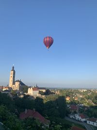 Hot air balloons flying over buildings in city against clear blue sky