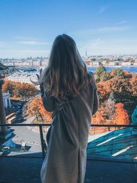 Rear view of woman standing at balcony against sky during winter