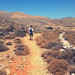 Rear view of man walking on mountain against clear sky