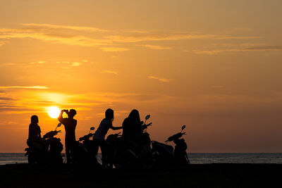 Silhouette people sitting on beach against sky during sunset