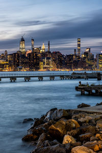 River by illuminated buildings against sky at dusk