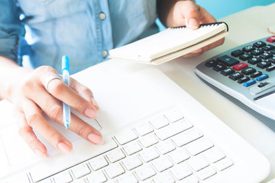 Midsection of woman holding book while using laptop