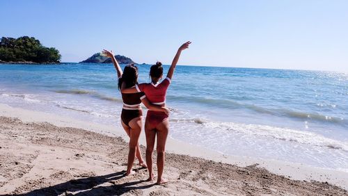 Rear view of women in swimsuit with arms raised standing on beach