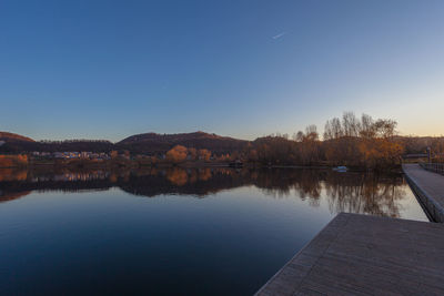 Sunset on hills reflected in the waters of lake with a hut on its banks and boat