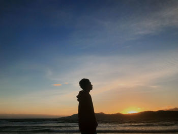 Silhouette man standing on beach against sky during sunset