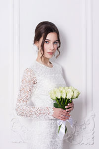 Portrait of beautiful bride standing against white wall