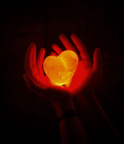 Close-up of hand holding apple against black background