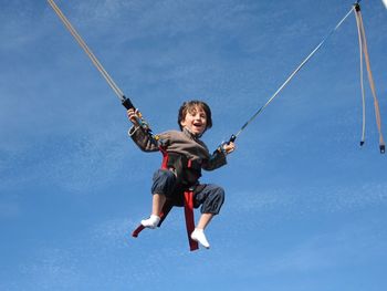 Low angle view of boy enjoying on bungee trampoline against blue sky