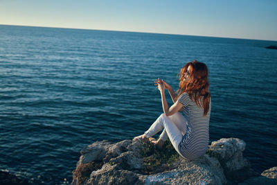 Woman sitting on rock by sea against sky