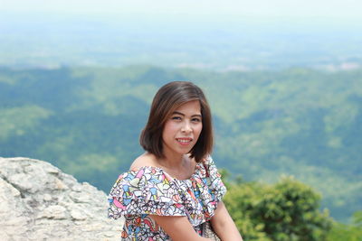 Portrait of smiling young woman standing against mountain