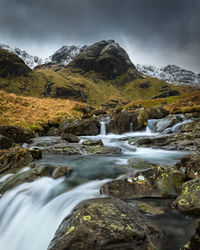 Stream flowing through rocks against sky