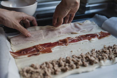 Crop person making roll with ham person