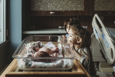 Sisters looking at newborn brother in hospital bassinet