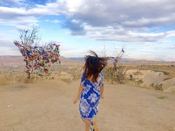 Rear view of woman running on field by multi colored fabrics on dry plants against sky