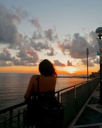 Rear view of man looking at sea against sunset sky