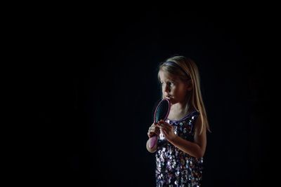 Girl holding comb while standing against black background